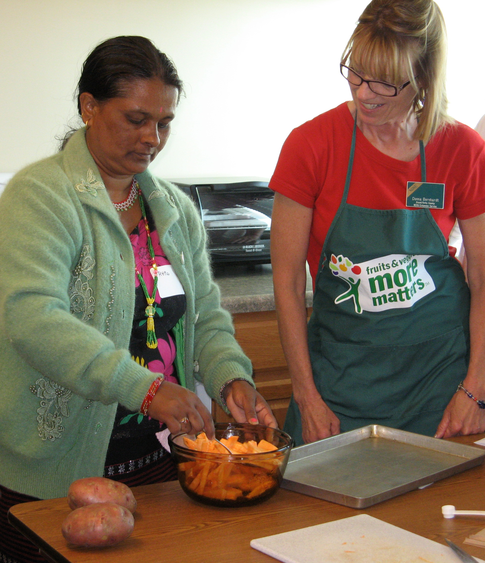 Grand Forks County Extension agent Donna Bernhardt, right, helps a woman make baked sweet potato fries during a cooking class for new Americans.