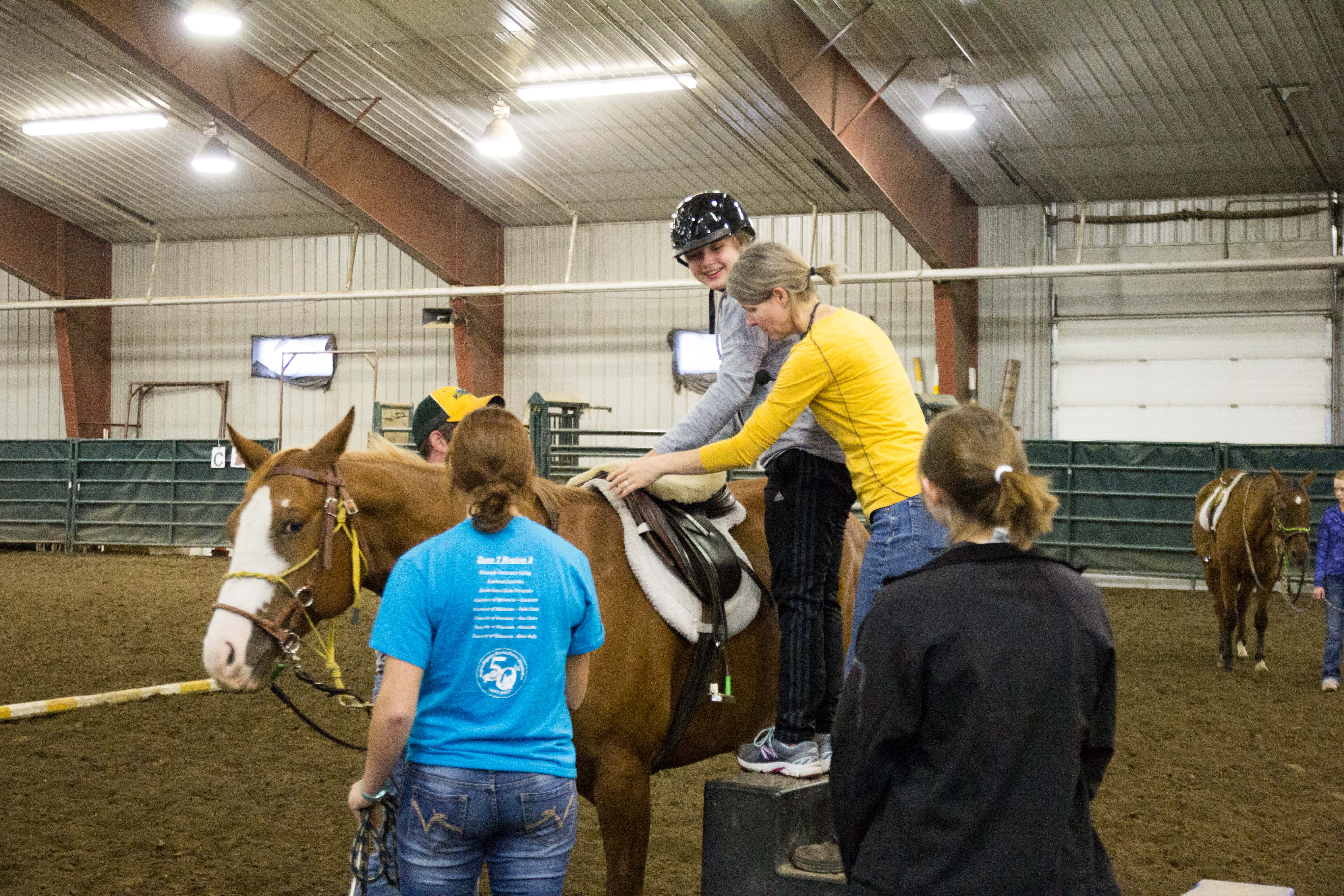 Erika Berg, NDSU associate professor and Bison Strides director, helps a girl mount a horse for her Equine-assisted Activities and Therapies program lesson. (Photo courtesy of Healthcare Equipment Recycling Organization of Fargo)