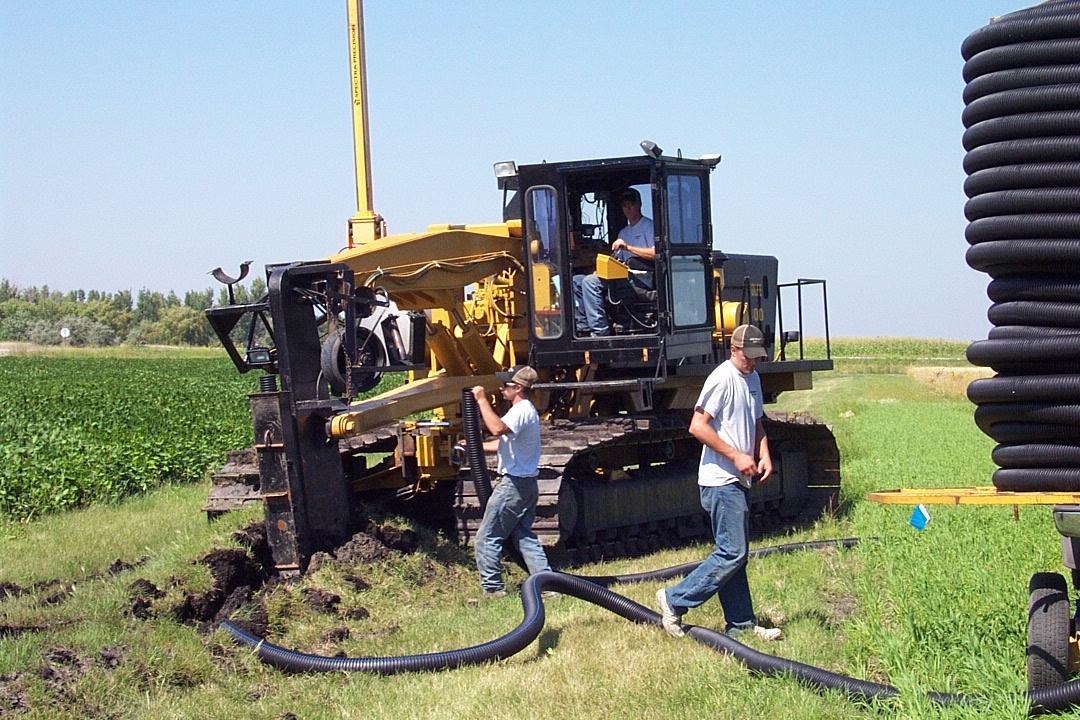 Workers connect tile to a plow. (NDSU photo)
